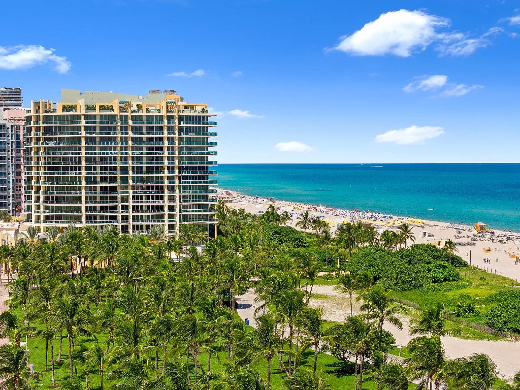 Exterior view of a modern luxury beachfront condominium in Miami Beach, showcasing sleek architecture with expansive glass balconies and lush palm trees, representing pet-friendly condos for sale.
