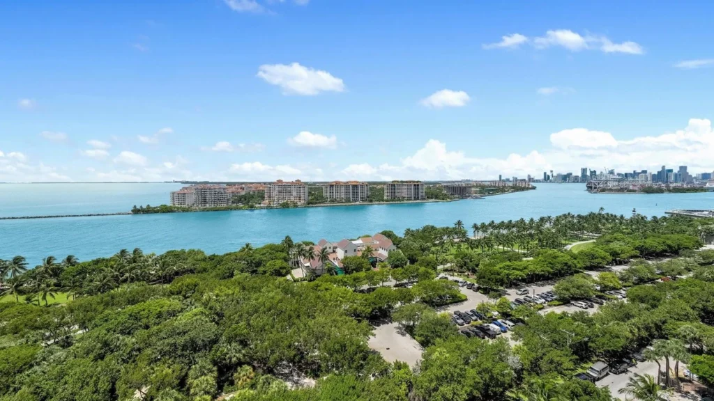 A stunning panoramic aerial view of South Pointe Park in Miami Beach's exclusive South of Fifth neighborhood, showing lush green spaces, winding pathways, the sparkling blue waters of Government Cut, and the Atlantic Ocean.